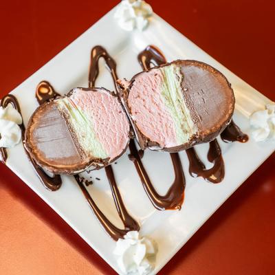 A sliced Neapolitan ice cream dessert with chocolate coating sits on a white plate.