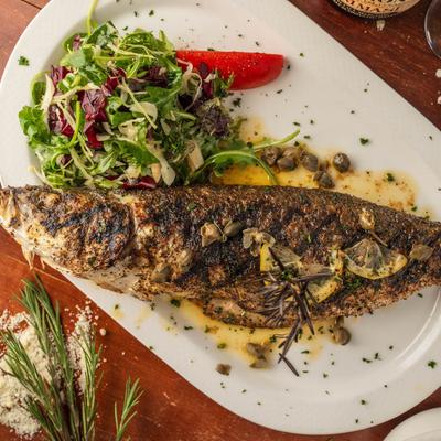 Whole grilled fish served alongside fresh greens.
