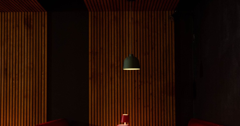 Dimly lit restaurant with wooden tables, red napkins and booth seats.