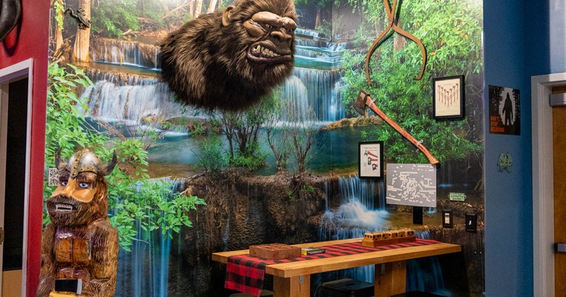 Area with faux gorilla mount, jungle waterfall wallpaper, table, and carved figure