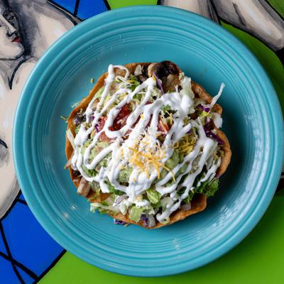 Taco salad in a crispy tortilla shell topped with shredded cheese and sour cream.