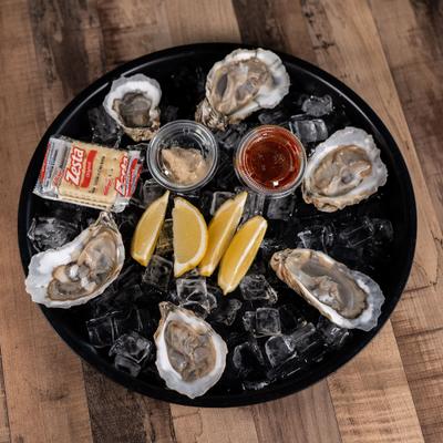 Platter of raw oysters served on a bed of ice with lemon wedges and condiments.