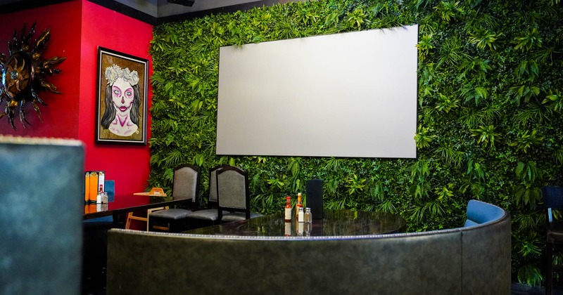 A private booth seating by artificial greenery wall with projection screen on it