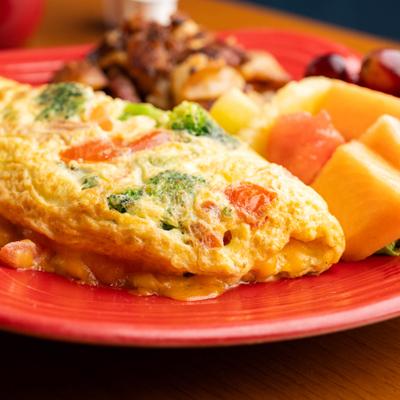 A vegetable omelet served on a red plate, with side home fries and fresh fruit.