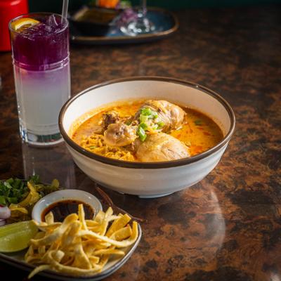 Northern Thai chicken Khao Soi curry noodle soup served with crispy sides and beverage.