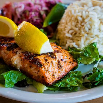 Grilled salmon, with lemon wedges on top, served with rice and red cabbage.