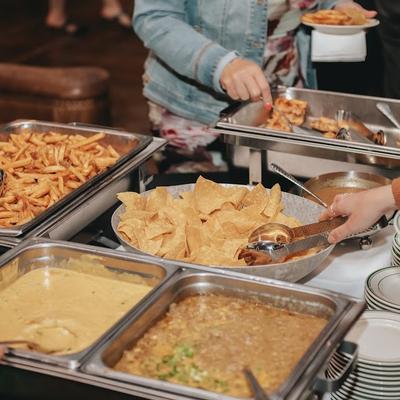 Guests serving themselves from a buffet table with fries, chips, and sauces.