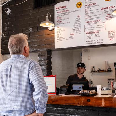 A customer looking at a menu above an order counter with staff.