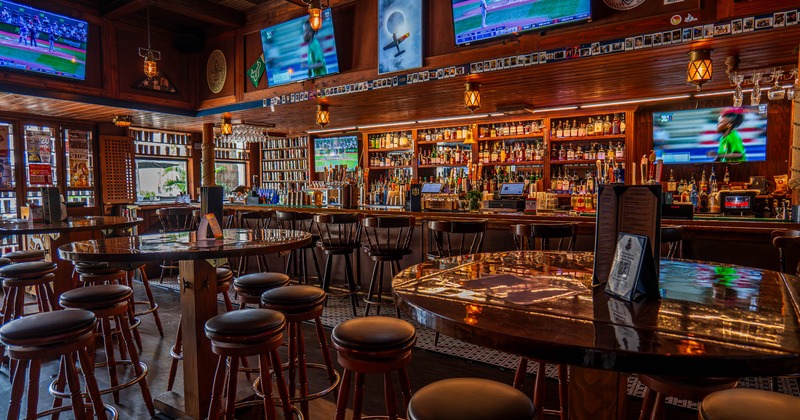 Interior, high seating wooden tables with padded stools, bar with drink shelves