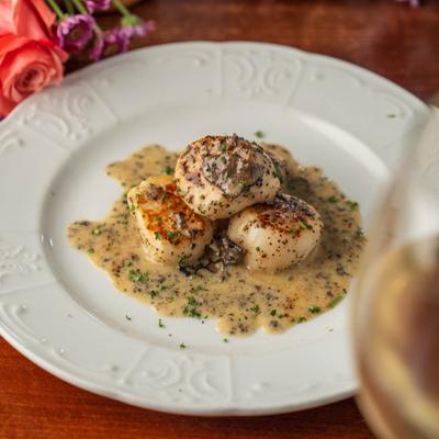 Seared scallops in truffle butter sauce on a white plate.