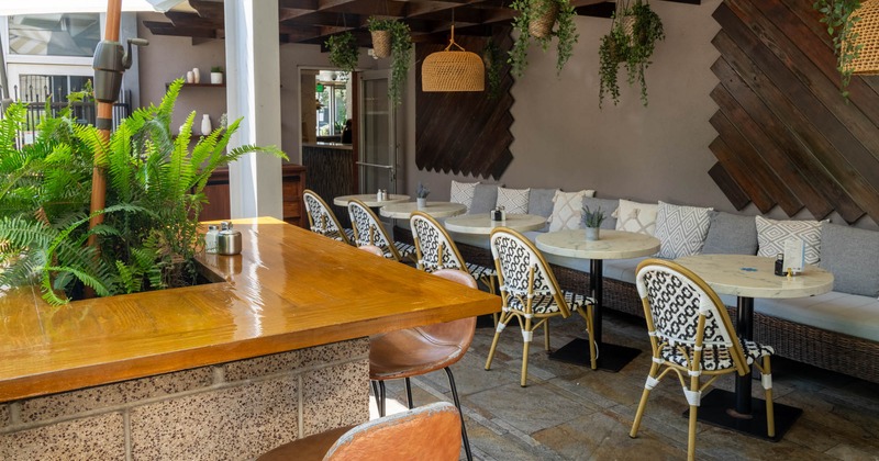 Outdoor seating area with wooden bar, wicker chairs, and hanging plants