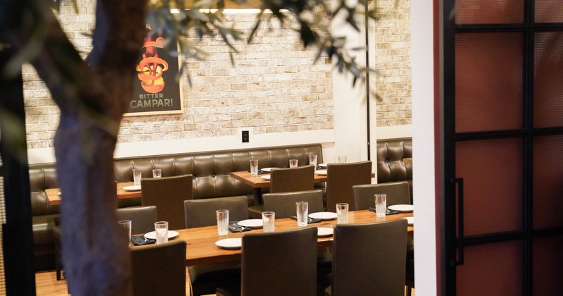 A restaurant dining area with wooden tables, brown upholstered chairs and a light brick wall.