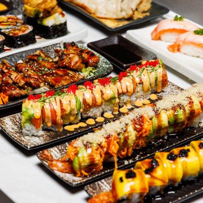 Variety of Japanese cuisine, including several maki sushi rolls topped with sauces.