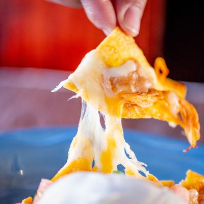 Cheesy tortilla chip being lifted with melted cheese stretching.