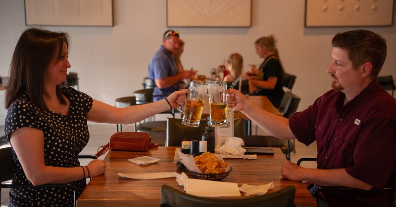 A couple holding large mugs of beer and toasting