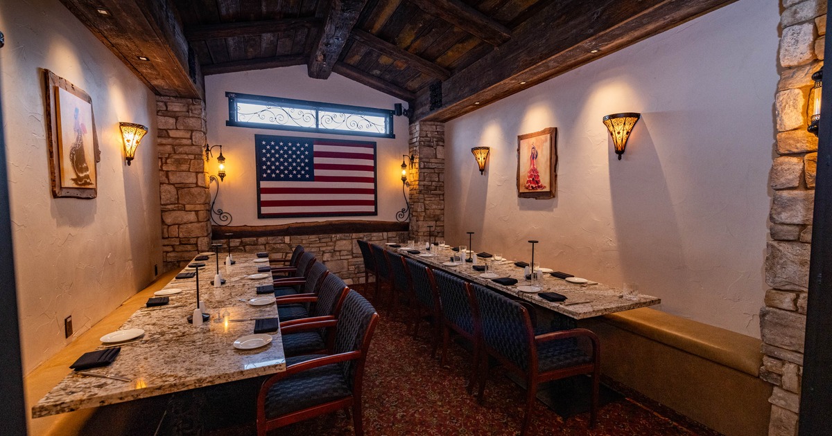 Rustic dining room with stone walls, large U.S. flag, long tables, and blue chairs
