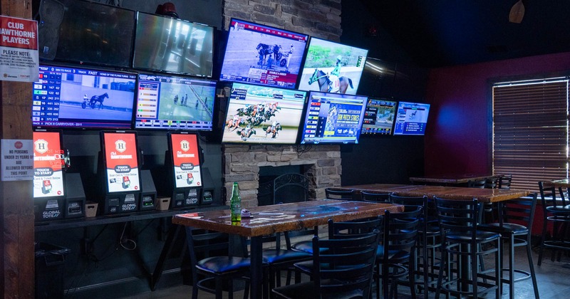 Interior of a sports bar with multiple screens showing horse racing and betting kiosks underneath