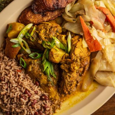 Curry chicken served with sides of rice and peas and cabbage.