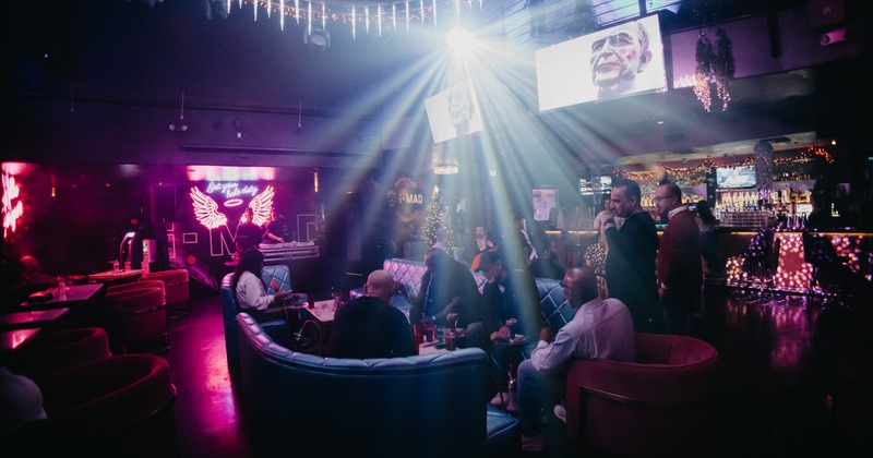 Seating booths surrounded with bar and tables, with neon signs