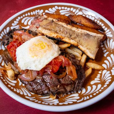 Ribeye steak topped with caramelized onions, fried egg, and a side of plantains.