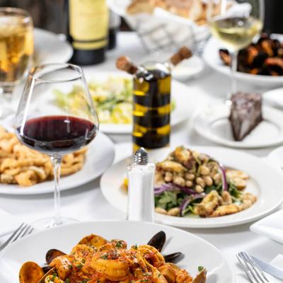 Seafood pasta in the foreground with wine, salads, seafood, and desserts in the background.