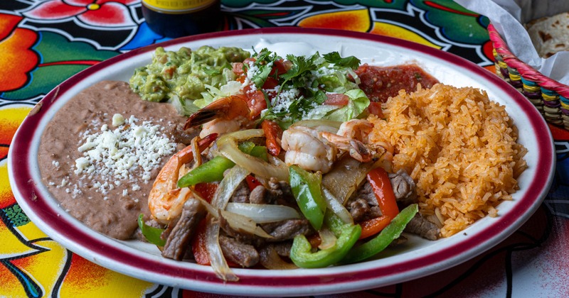 Steak and shrimp fajitas served alongside rice, beans, guacamole, and salsa