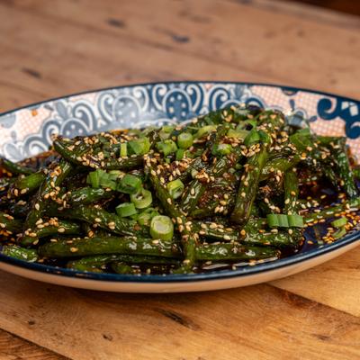 Cantonese green beans with sesame seeds and scallions on a patterned plate.