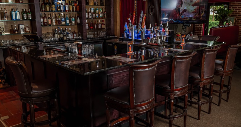 Upscale bar interior with a U-shaped granite counter, leather stools and a stocked liquor shelf