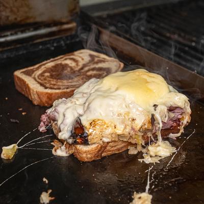 Reuben sandwich being prepared on a flat-top grill.