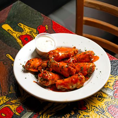 A plate of buffalo wings with dipping sauce on a colorful table.