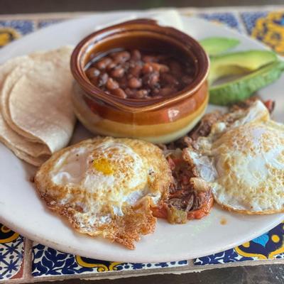 Fried eggs, black beans with slices of avocado served on a white plate