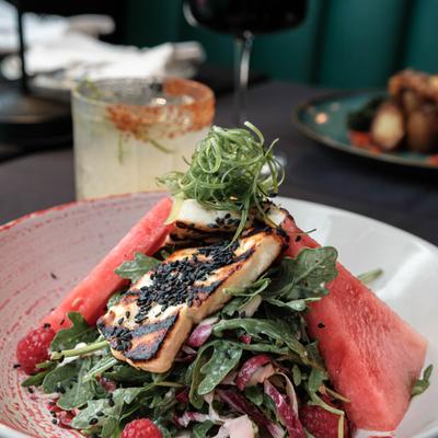 Raspberry and watermelon salad on a table with drinks and dishes.