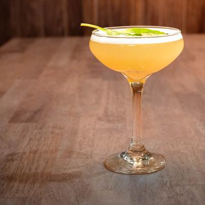 A light orange cocktail served in a coupe glass.