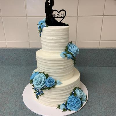 A three tiered wedding cake adorned with blue roses and a silhouette of a couple wedding cakes