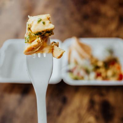 A bite of food on a fork, and a take away dish in the background.