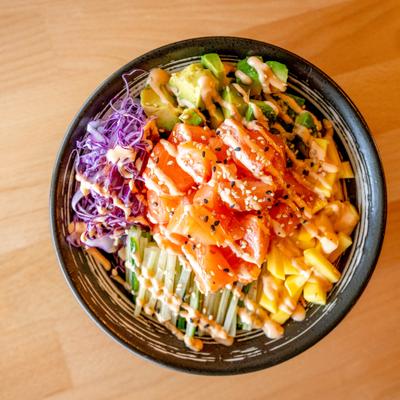 Salmon poke bowl with vegetables, diced mango and a drizzle of sauce.