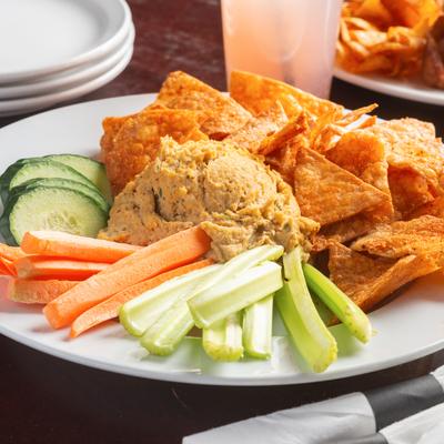 Hummus with chips, celery, carrots, and cucumber on the plate.