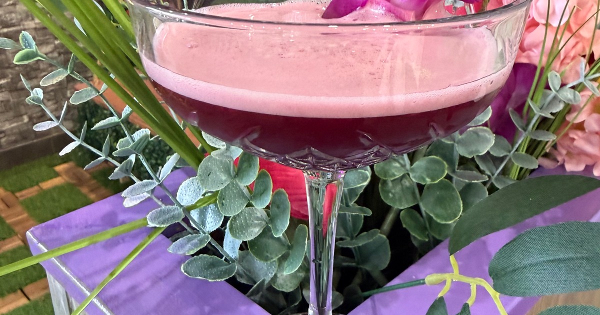 A deep purple cocktail with pink foam served in a crystal coupe