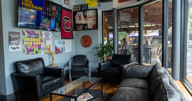 A cozy sports bar lounge featuring black leather seating, memorabilia, and large windows
