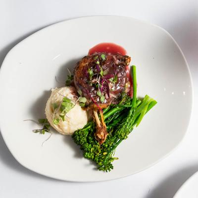 Duck leg served with mashed potatoes and broccolini, garnished with micro greens.