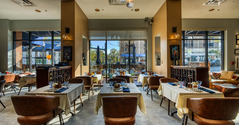 A cozy interior with tables and chairs, large windows and pendant lights.