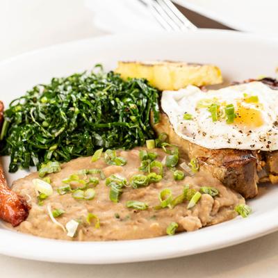 Grilled pork chop, fried egg, pureed beans, collard greens, and sausage.