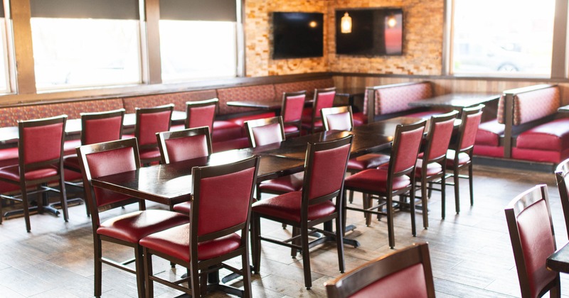 Interior dining area with red cushioned chairs, wooden tables, booth seating, and mounted TVs