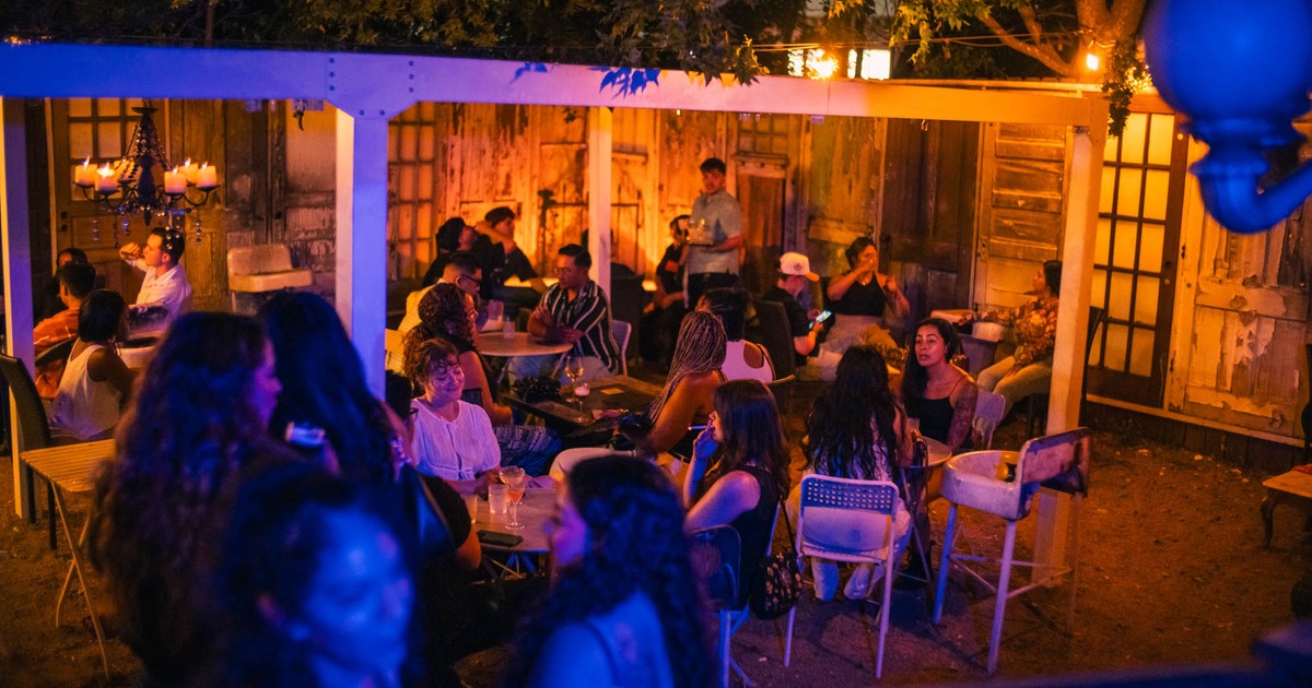 Outdoor nighttime gathering with people seated at tables under warm lights