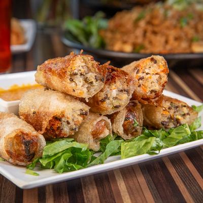Crispy fried spring rolls stacked on a plate with fresh greens.