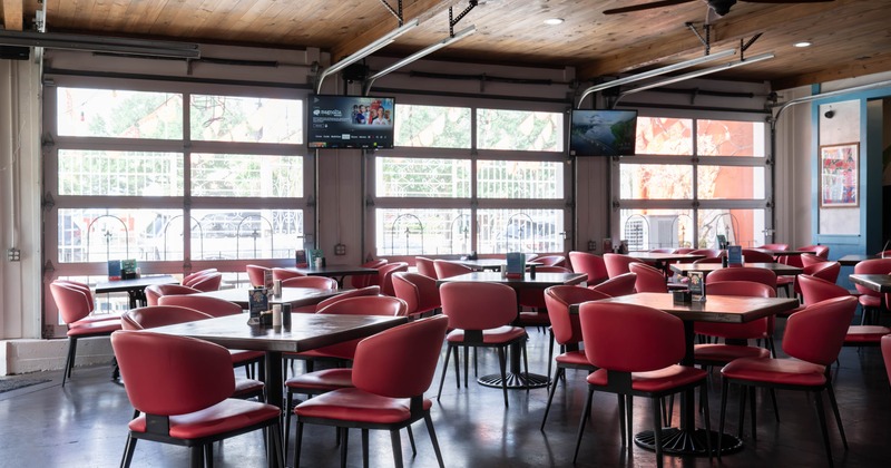 Inside, dining room with red chairs, dark tables, wall-mounted televisions