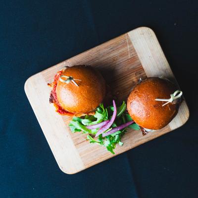 Two sliders on a wooden board, accompanied by fresh greens.