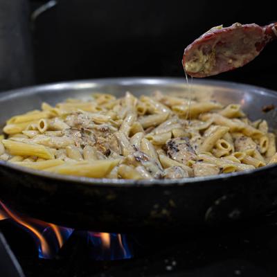 Creamy pasta with sauce in a pan on a gas stove.