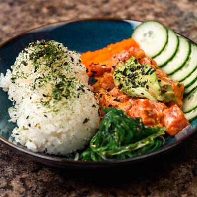 Salmon poke bowl with white rice, avocado slices, seaweed, cucumber slices, and orange roe.