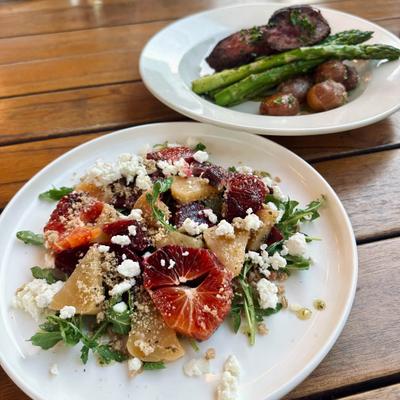 A beet salad and a dish of sliced steak with roasted small potatoes, and asparagus.